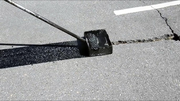 Hot-rubber crack filler being squeegeed into an asphalt crack